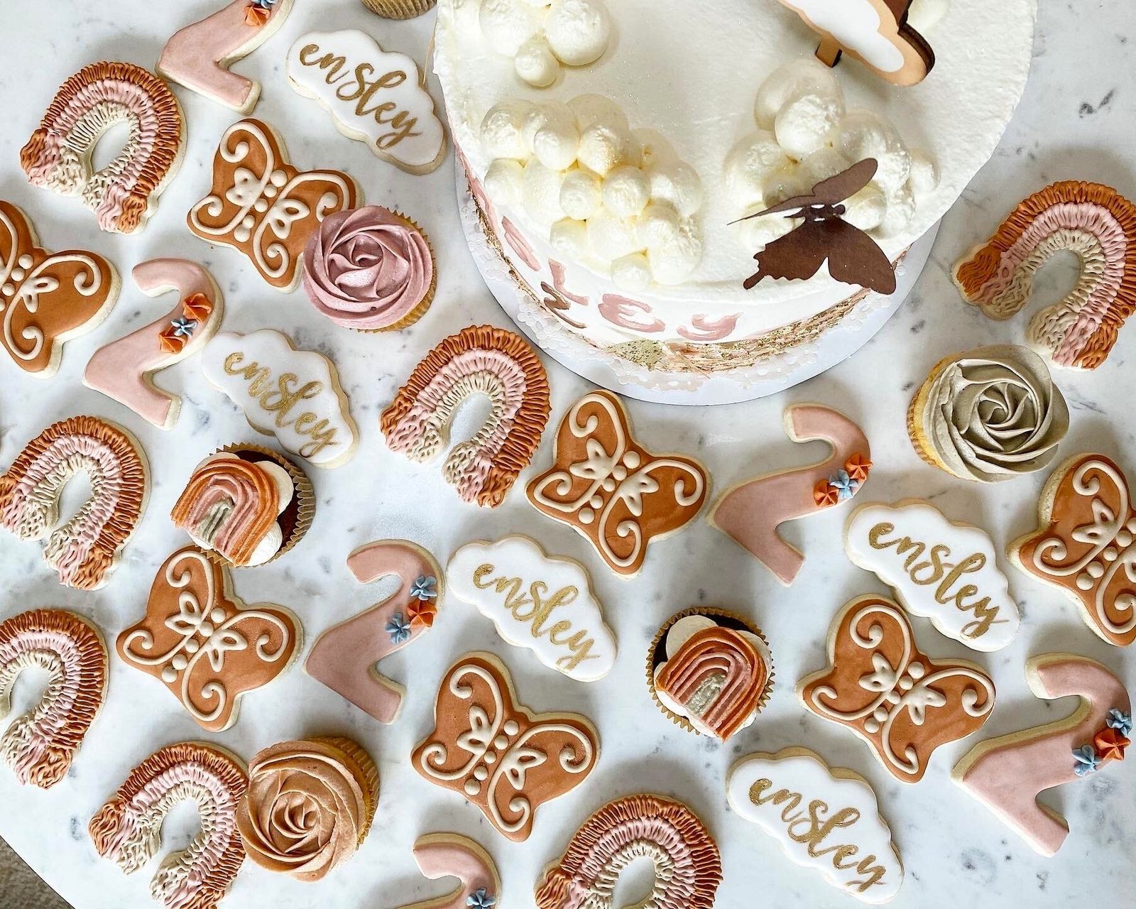 Decorated sugar cookies with rainbows, butterflies and a name, around a birthday cake