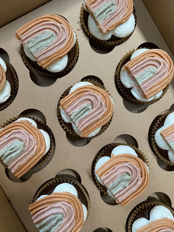A dozen cupcakes topped with pastel buttercream rainbows