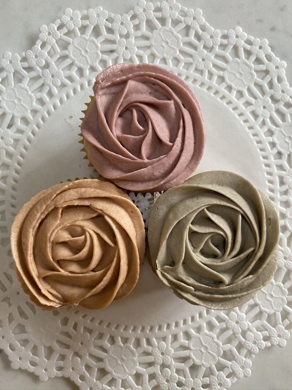 Three rosette cupcakes in mauve, gold and sage on a doily