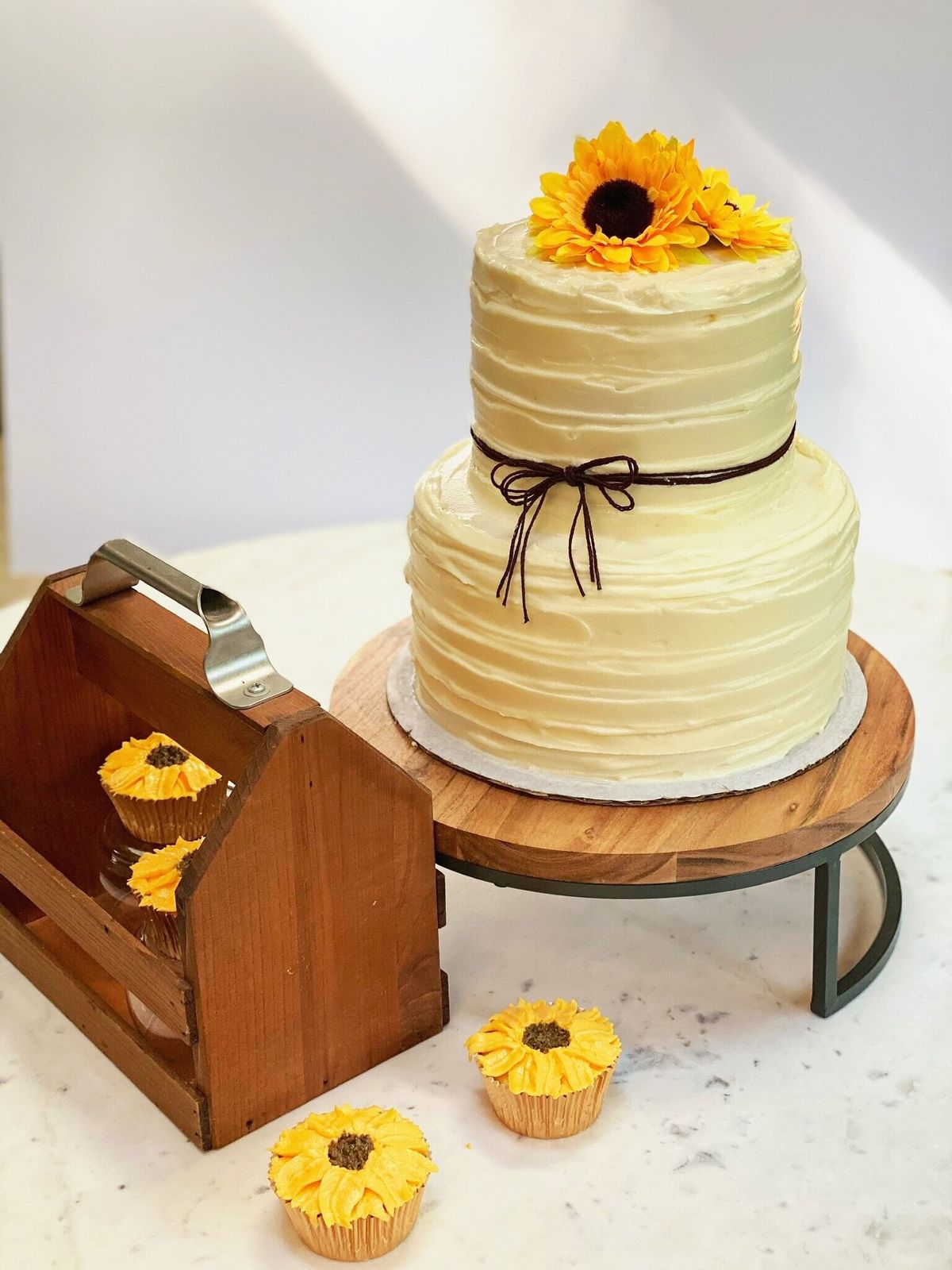 Two-tier buttercream cake topped with a sunflower, with matching sunflower cupcakes